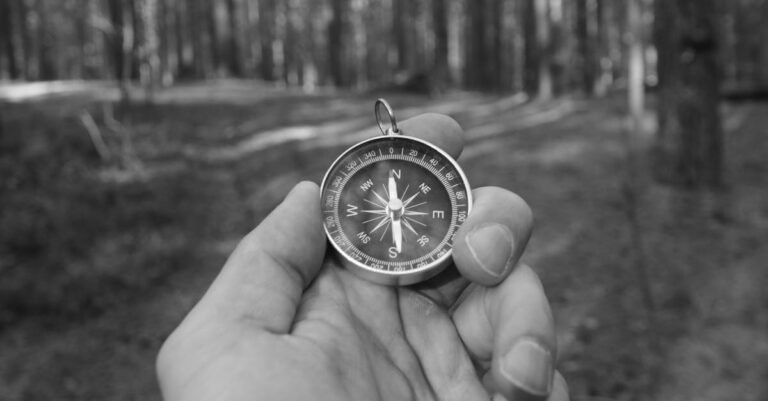 A black and white photo of a man holding a compass during a forest exploration, symbolizing navigation.