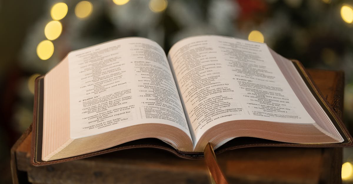 Open Bible resting on wooden surface with blurred festive background lights.