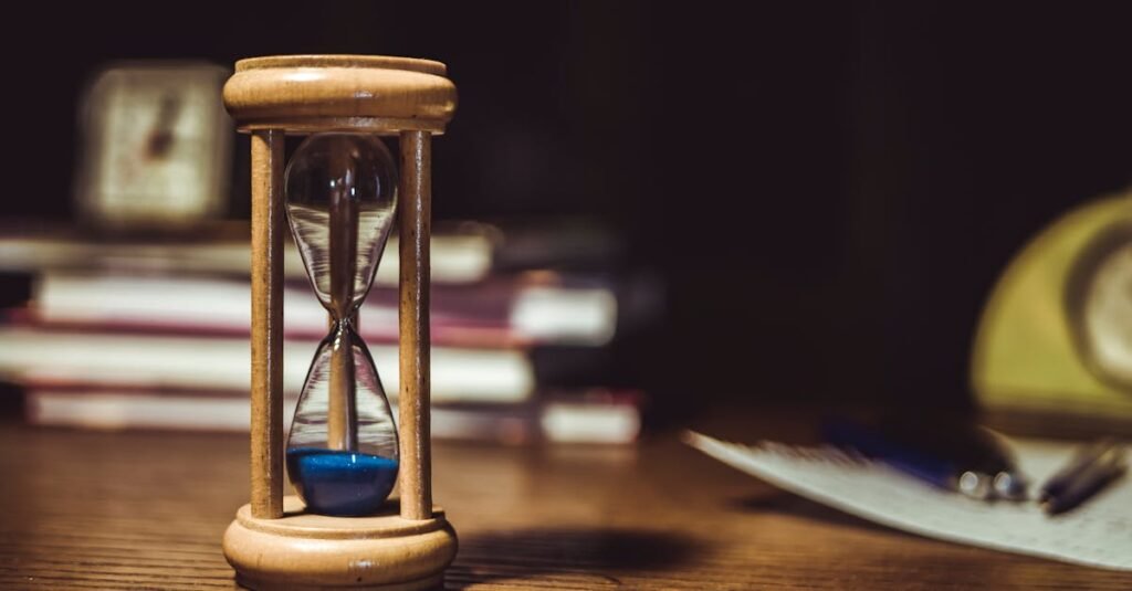 A close-up of a wooden hourglass with blue sand on a wooden desk, symbolizing time and patience.