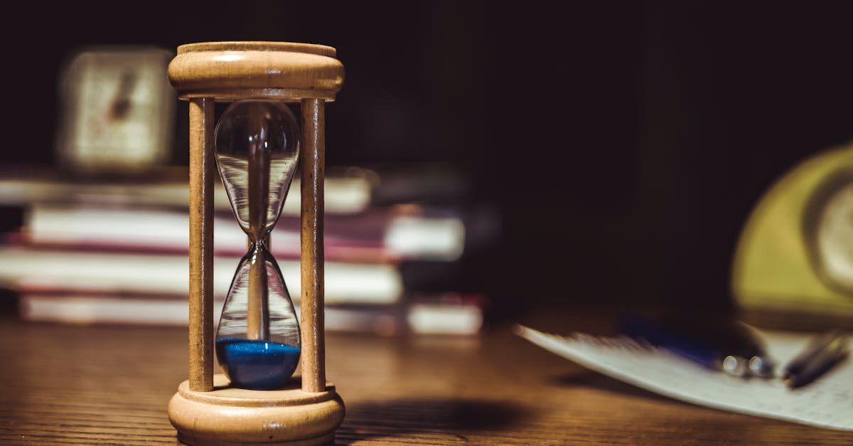 A close-up of a wooden hourglass with blue sand on a wooden desk, symbolizing time and patience.