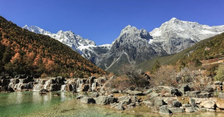 Scenic view of waterfalls cascading with snow-capped mountains under clear blue skies.