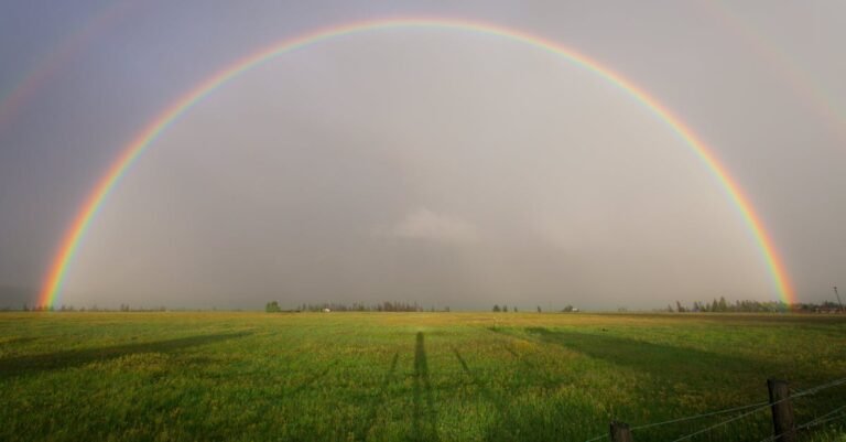 A full rainbow arches over a serene farmland landscape, capturing natural beauty.