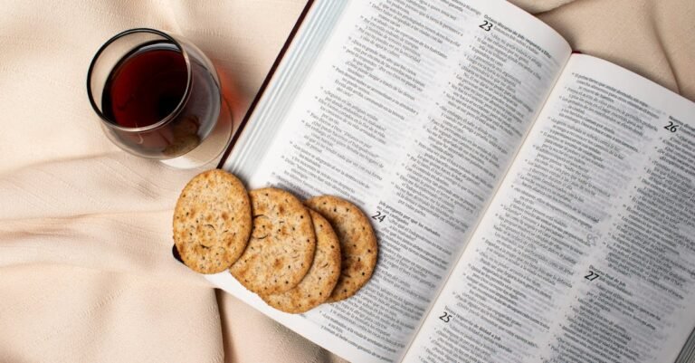 Flat lay of an open Bible with a glass of wine and cookies on a soft textile surface.